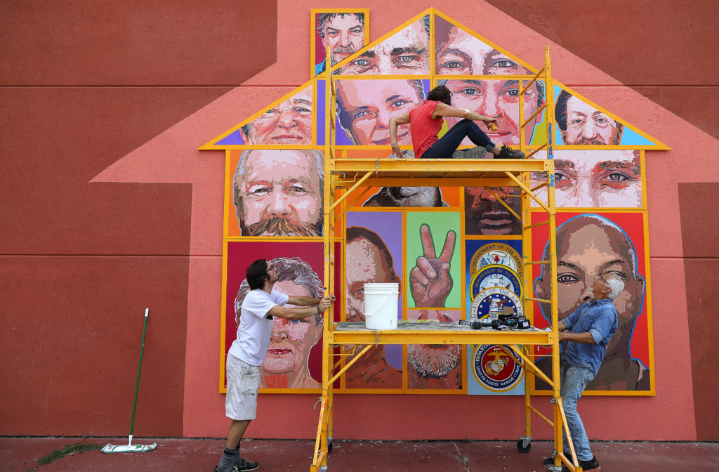 Artists Daniel Doughty, left, and Mario Uribe, right, move a scaffolding holding Jennifer Tatum, so that she can reach another portion of the Palms Inn Project mural, in Santa Rosa on Tuesday, September 12, 2017. The mural is installed on the west side of the Palms Inn, facing Highway 101. (Christopher Chung/ The Press Democrat)
